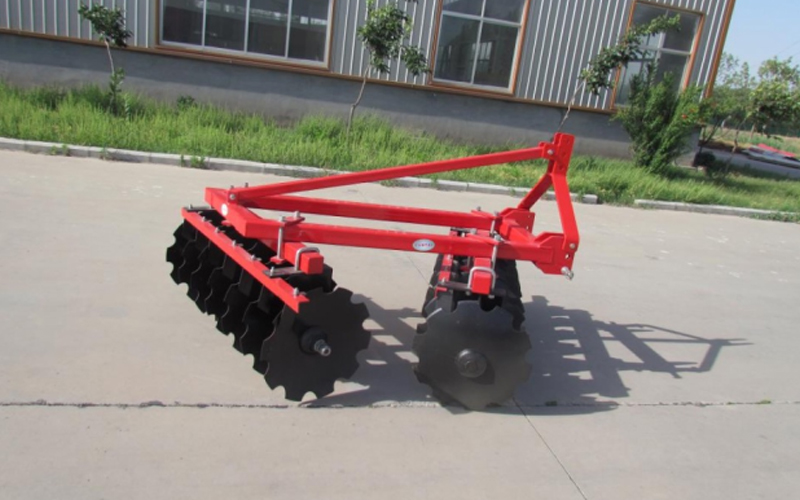 Một chiếc bừa đĩa màu đỏ có nhiều đĩa được đậu trên mặt đường lát đá